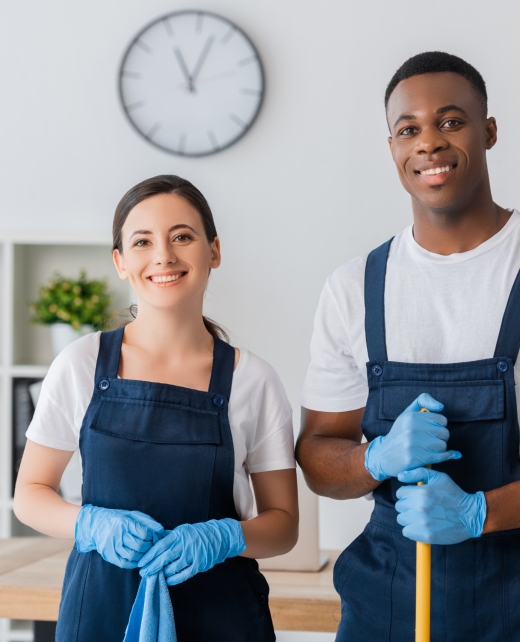 Smiling multiethnic workers of cleaning service holding rag and mop while working in office